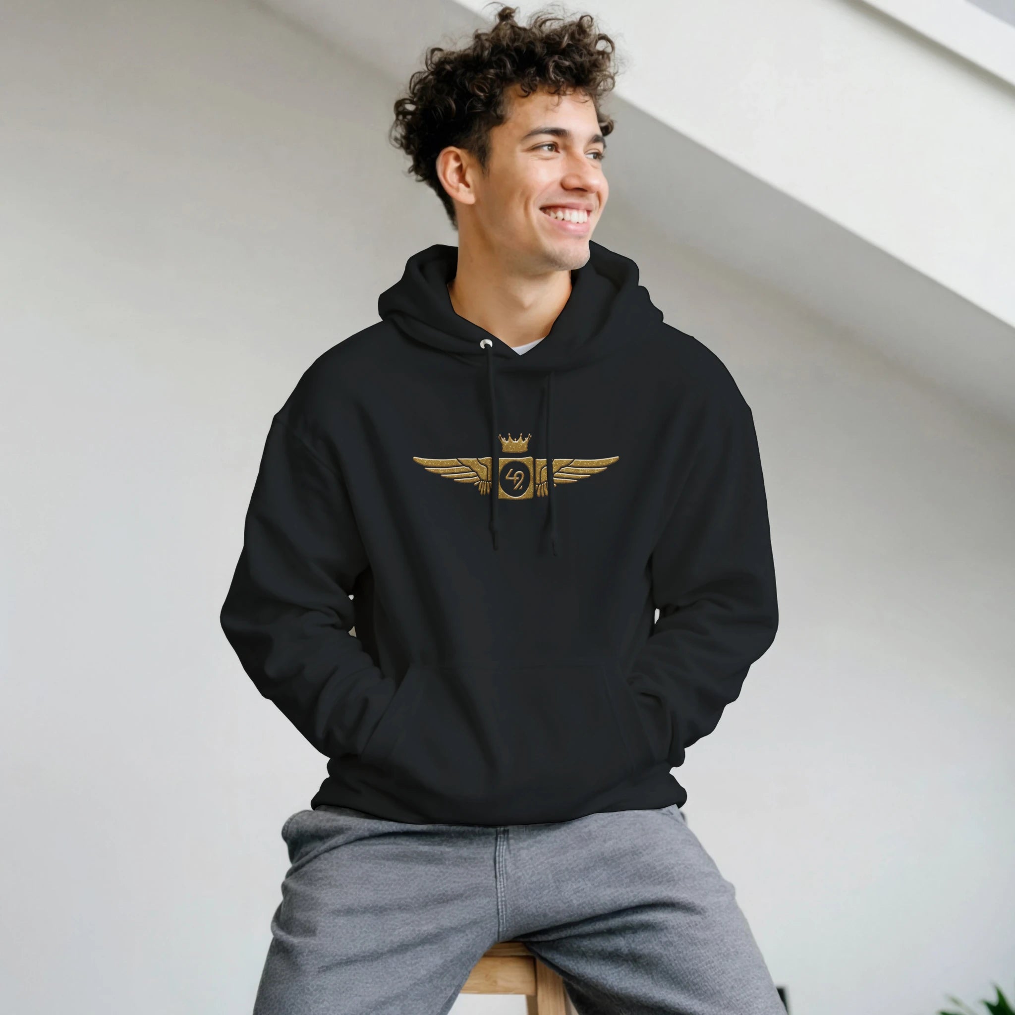Joven con sudadera negra con un diseño exclusivo de alas doradas en el pecho, símbolo de modernidad y estilo. Perfecta para los amantes del arte conceptual y el diseño único.